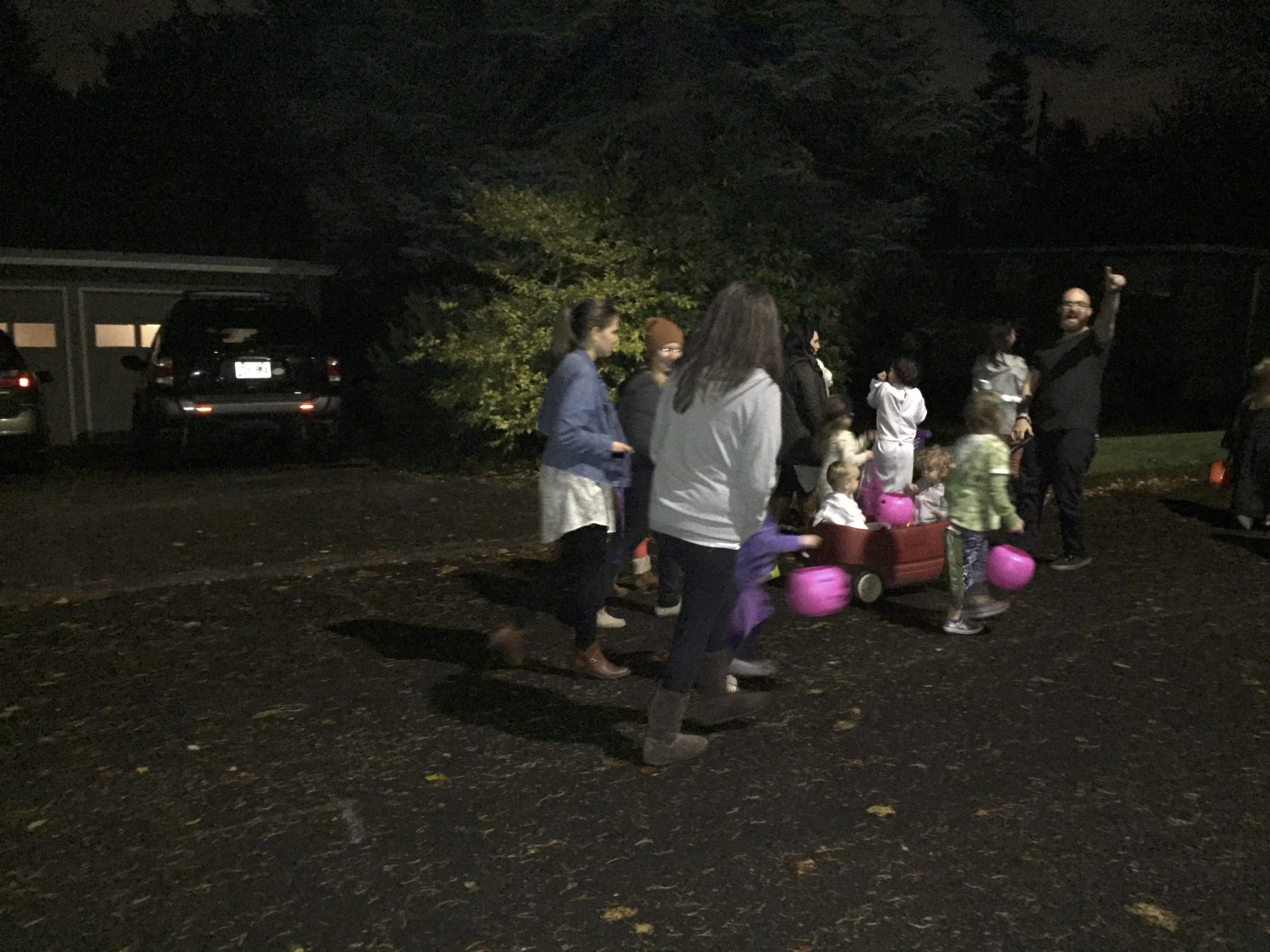 Children carrying treat buckets with adults outdoors at night