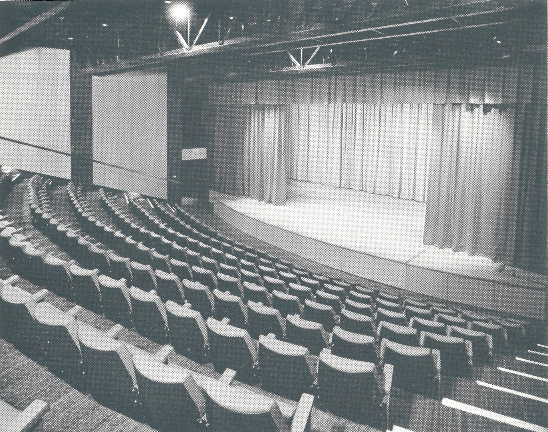 Wide view of an auditorium stage with a closed curtain and rows of seats